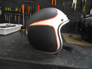 Capacete de lado feito por nós em preto fosco e uma pintura branco semi-brilho dando um movimento do vento para traz, chegando ao logotipo da Harley-Davidson.