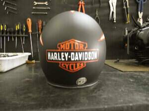 Capacete feito por nós visto de traz em preto fosco e uma pintura branco semi-brilho dando um movimento do vento para traz, chegando ao logotipo da Harley-Davidson.