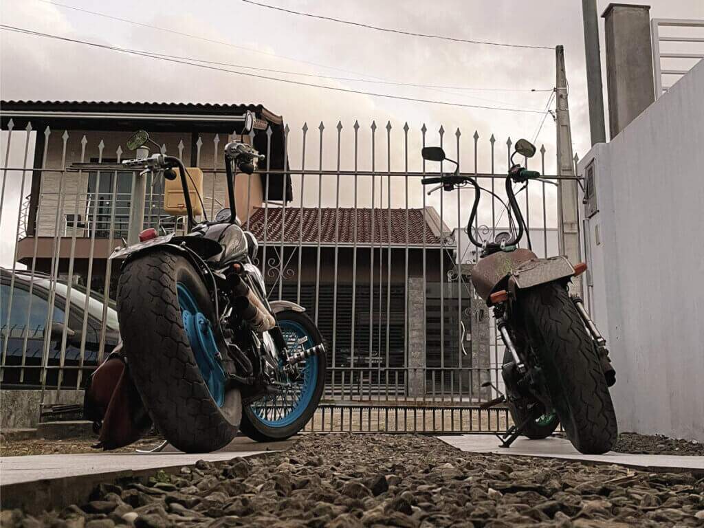 Duas motos em frente ao portão. Uma Yamaha Virago 250 customizada e uma Honda Shadow 600 também toda customizada.