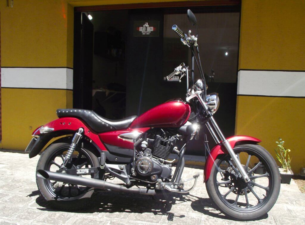 Red Pearl vista pela lateral direita, possibilitando ver seu escapamento de 6" que vai até o final do pneu traseiro, seu guidão Ape-Hanger de 14", comando avançado e sua pintura vermelho cereja brilhante.